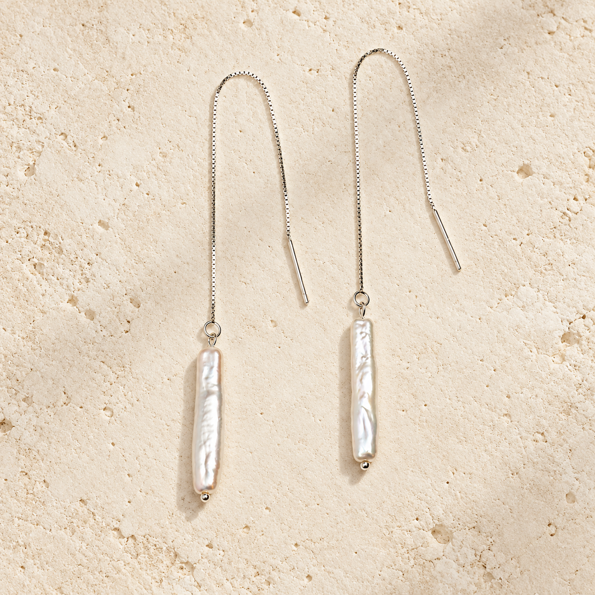 Moon Letter white pearl threader earrings on warm ivory stone